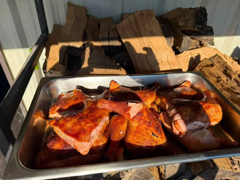 Pan of smoked chicken in front of stacked firewood