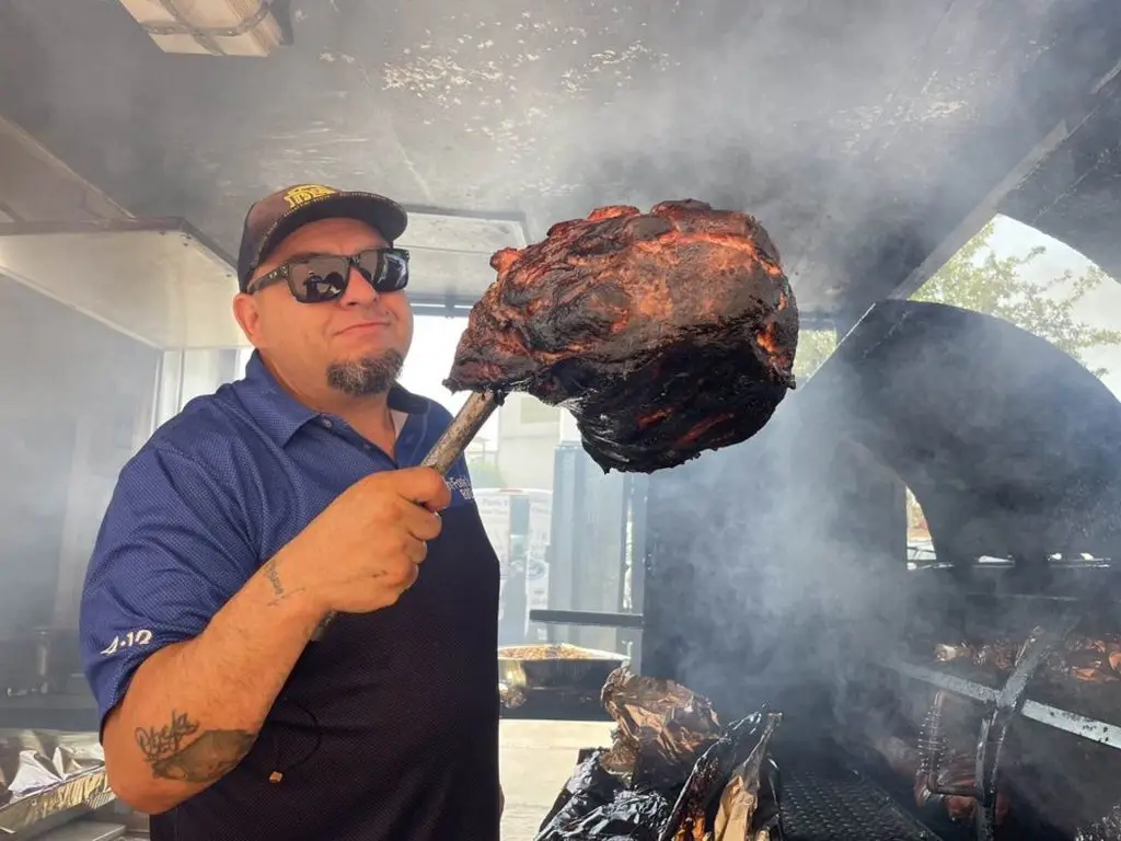Pitmaster Angel Espinoza holding a smoked beef rib in the smoke